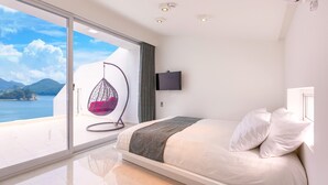 A modern bedroom with a bed, a hanging chair, a TV, and a large window with a view of the sea and mountains. - Geoje Star Marine Pool Villa Pension - V (Geoje)