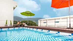 En pool på taket med ett rutmönstrat kakel, två solstolar och ett grönt parasoll.