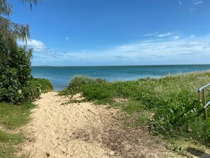 Un sentier sablonneux qui mène à une plage d’où l’on a une vue dégagée sur l’océan.