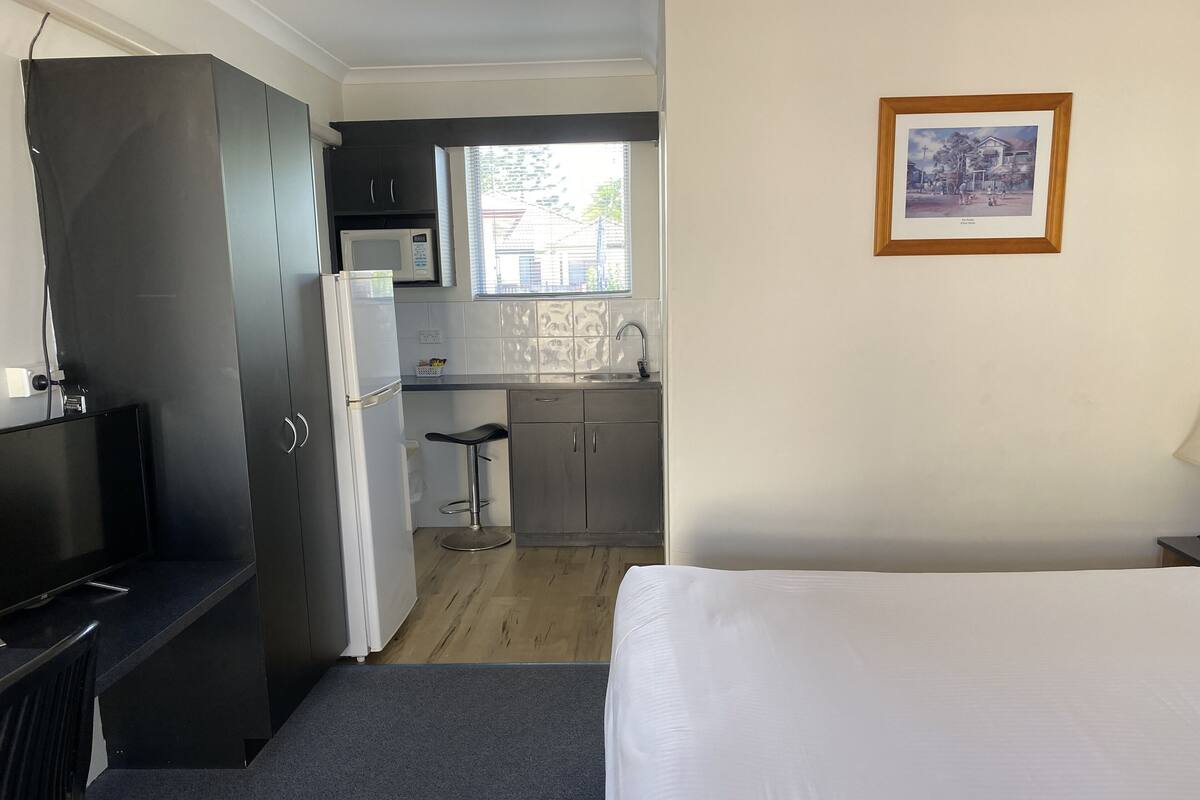 Quarto de hotel compacto com cama, cozinha compacta, guarda-roupa escuro e pequeno espaço bar.