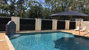 A swimming pool with clear water, surrounded by a fenced area with a decorative wall and a covered seating area with chairs. - Hervey Bay Motel (Urangan)