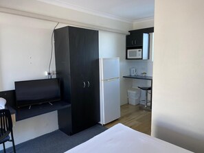 A compact room with a bed, a black wardrobe, a white refrigerator, a microwave, and a small kitchenette area. - Hervey Bay Motel (Urangan)
