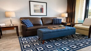 Una sala moderna con un sofá de cuero marrón, un otoman azul y una alfombra estampada.