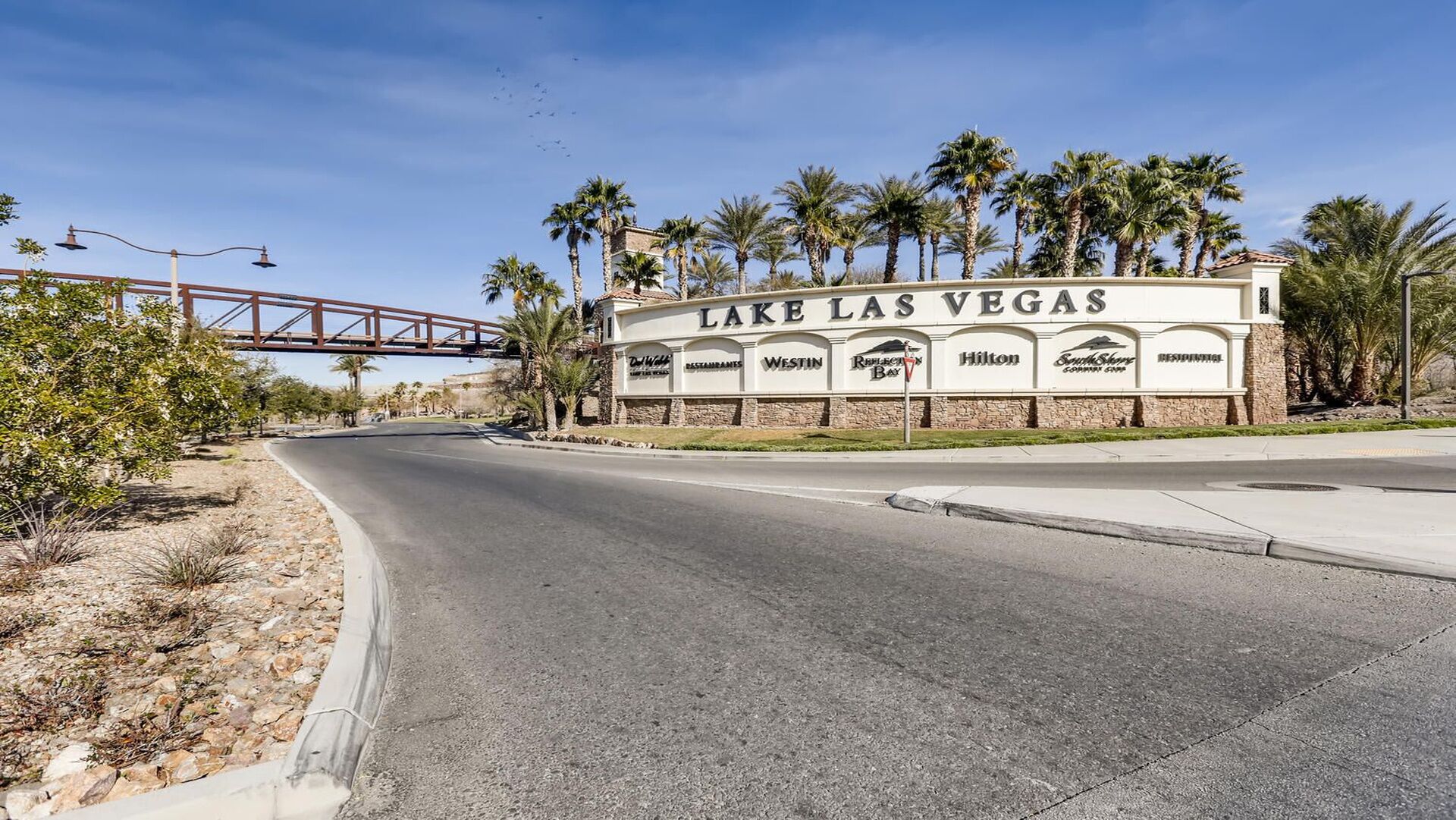 Una carretera que lleva a un hotel llamado 'Lake Las Vegas', con cielo despejado y palmeras.