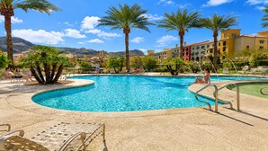 A swimming pool with lounge chairs and palm trees, surrounded by buildings with Mediterranean architecture. - Lake Las Vegas condo with balcony, lake and golf course view (Henderson)