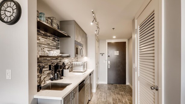 A modern kitchen with a sink, stove, microwave, and cabinets. There is a clock on the wall and a door with a sign. - Lake Las Vegas condo with balcony, lake and golf course view (Henderson)