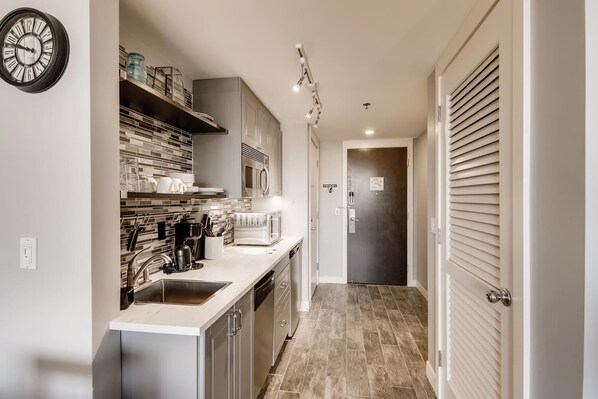 A modern kitchen with a sink, stove, microwave, and cabinets. There is a clock on the wall and a door with a sign. - Lake Las Vegas condo with balcony, lake and golf course view (Henderson)