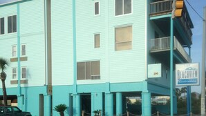 Un immeuble turquoise à plusieurs étages, doté de balcons, d’un parking et d’un panneau de signalisation indiquant « Beachview Condominiums ».
