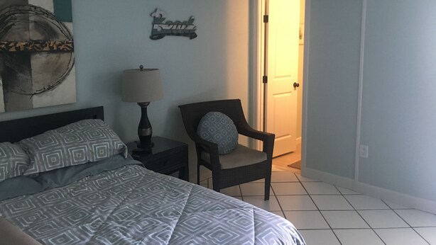 Une chambre à coucher avec un lit, une table de chevet avec une lampe, une chaise et une porte donnant sur une autre pièce.
