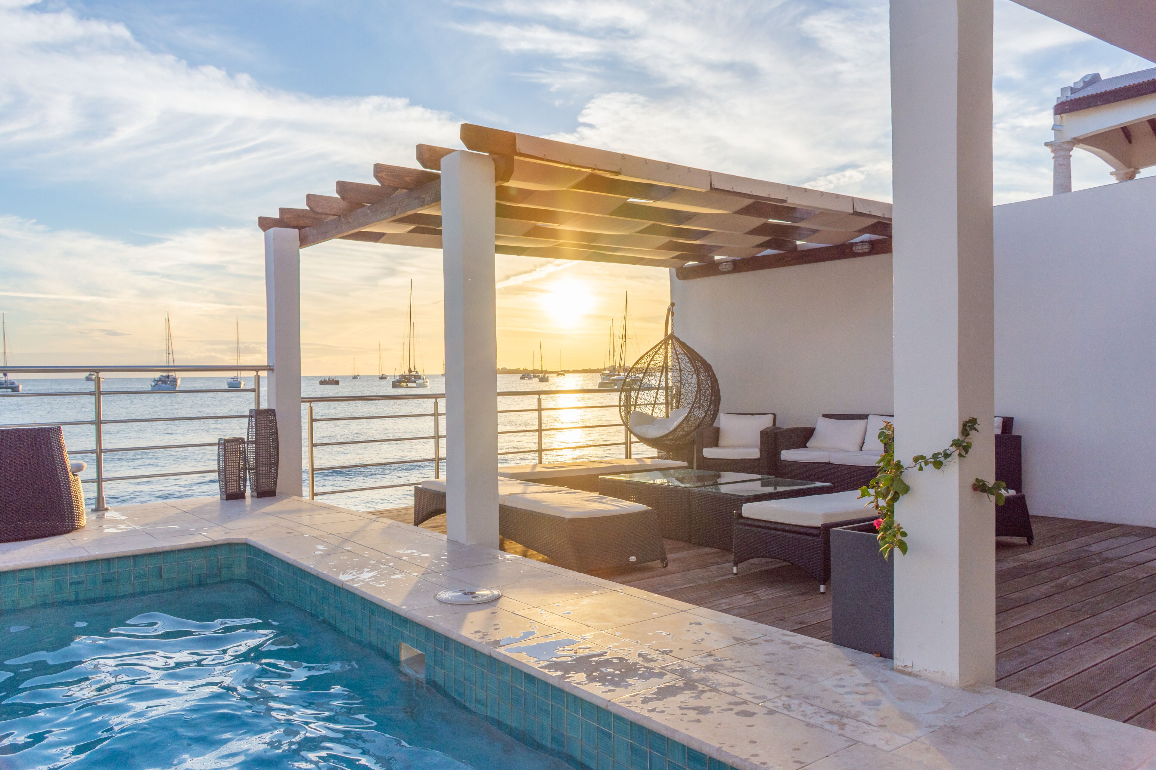 Un espace aménagé au bord de la piscine, avec une pergola, des chaises longues et une vue sur la mer au coucher du soleil.