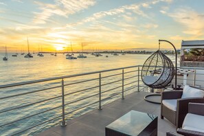 Terraço com vista para o mar e para o pôr do sol, com móveis de vime e uma cadeira suspensa.