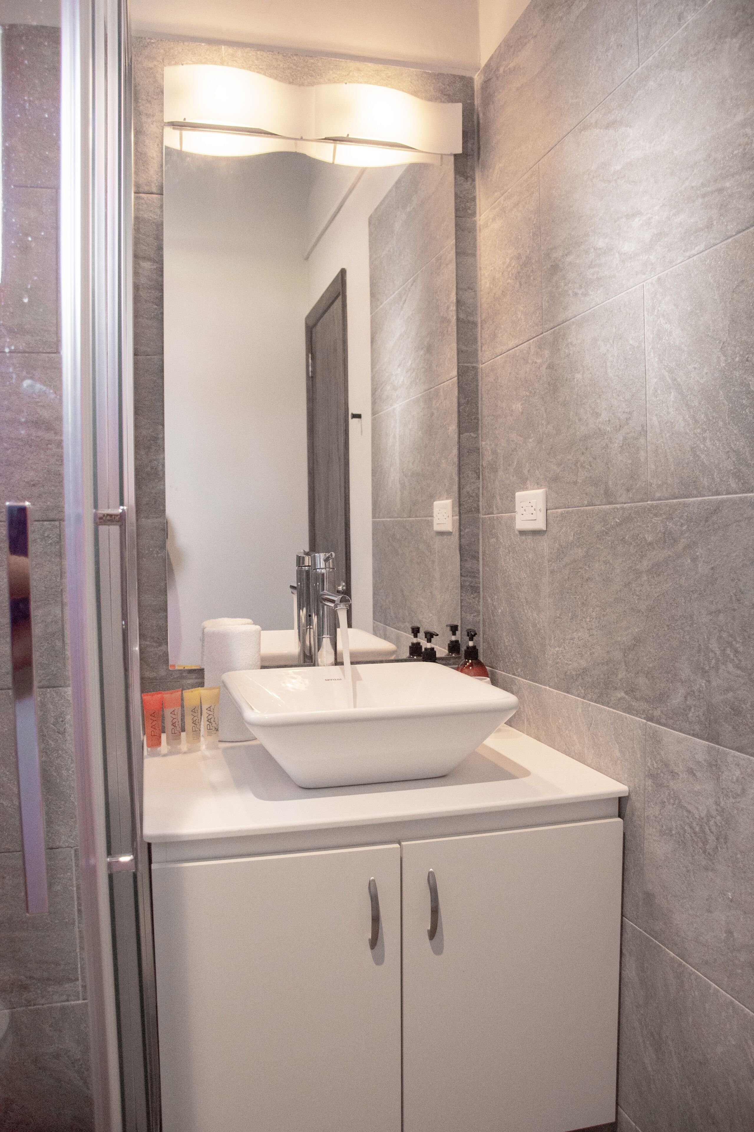 A modern bathroom with a white sink, a large mirror, and grey tiled walls.