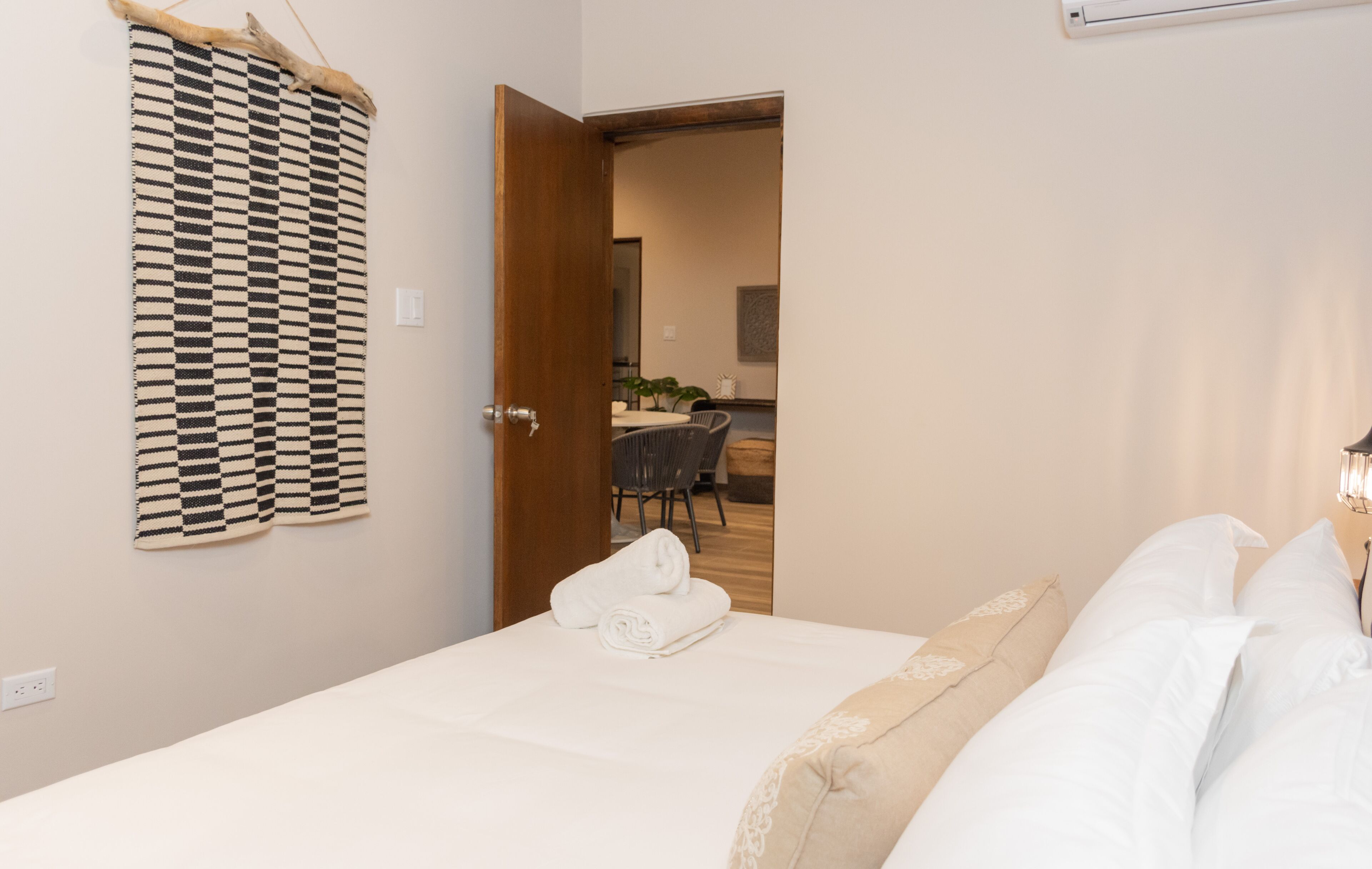 Ein Hotelzimmer mit einem Bett, einem an der Wand befestigten Schachbrettteppich, einer Tür zu einem Essbereich und einer Nachttischlampe.