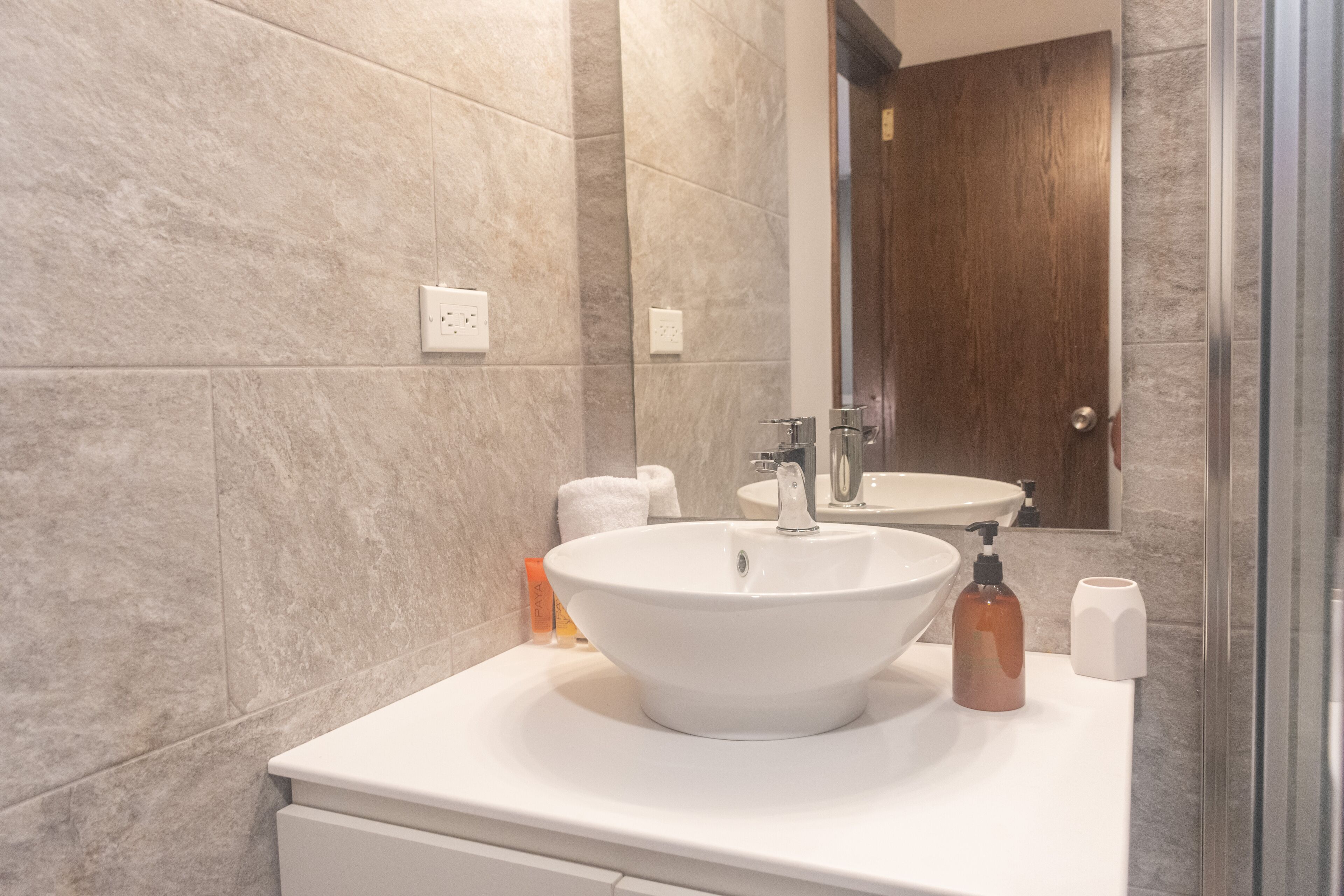 A modern bathroom with a large white sink, a mirror, and a shower area.