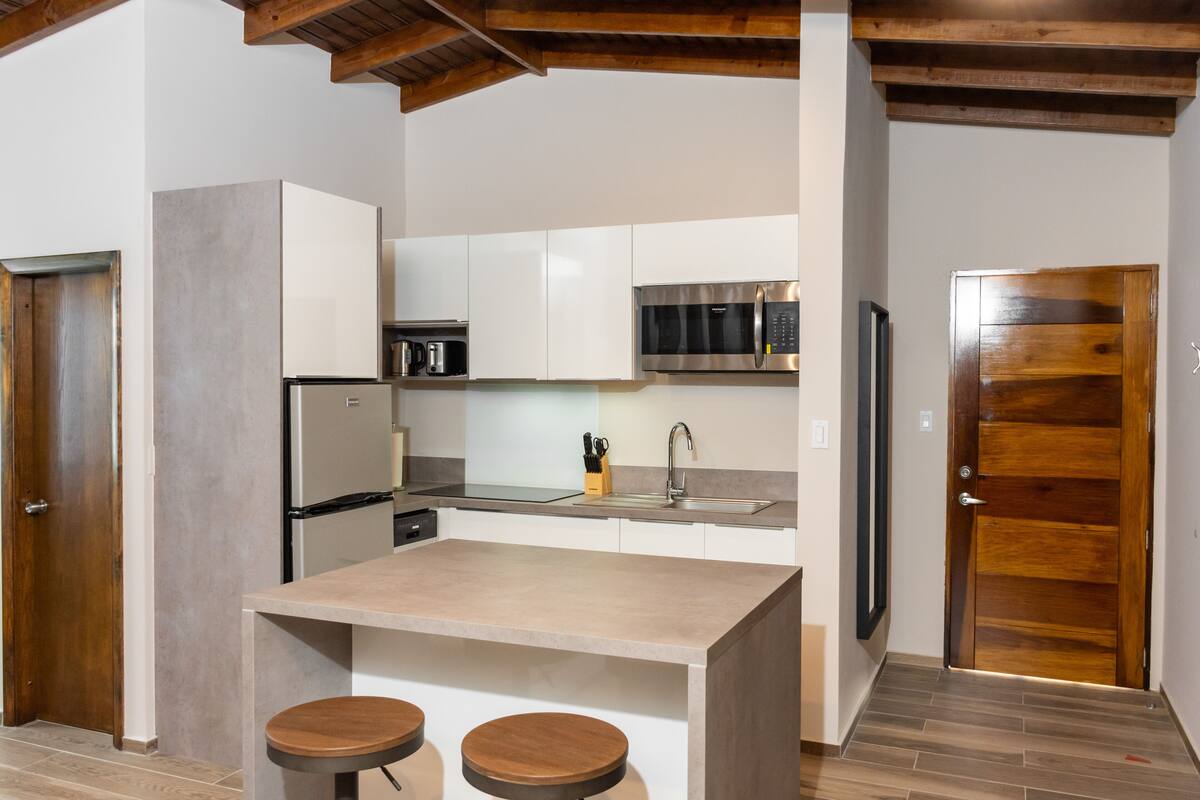 A modern kitchen with white cabinets, a stainless steel refrigerator, a microwave, and a wooden door.