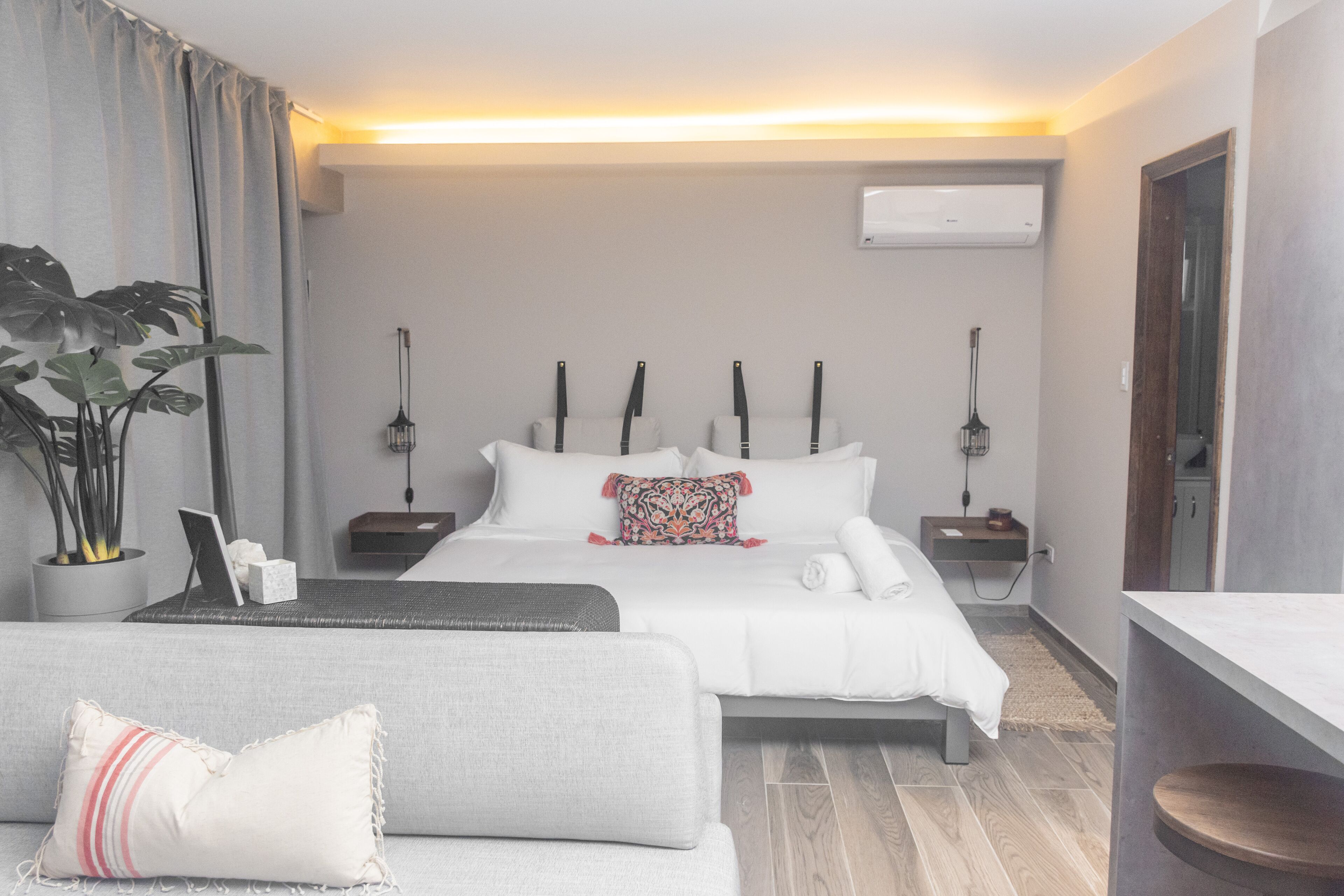 Una habitación de hotel moderna con una cama grande, mesitas de noche, un sofá y una planta en maceta.