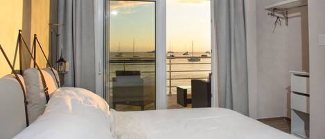 Une chambre d’hôtel avec un lit, une chaise, une table et une vue sur les bateaux qui naviguent, visible par une porte ouverte.