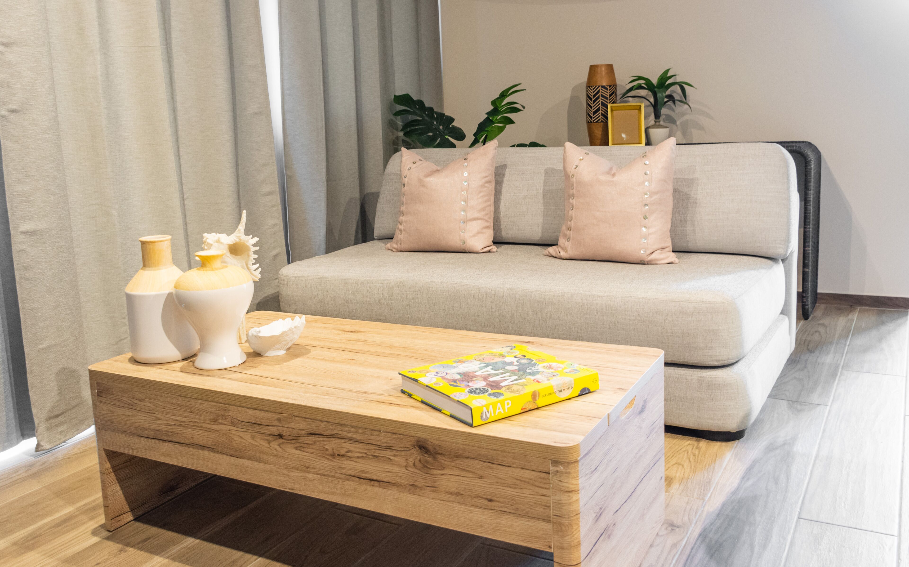Een moderne woonkamer met een bank, decoratieve kussens, een houten salontafel en een boek.