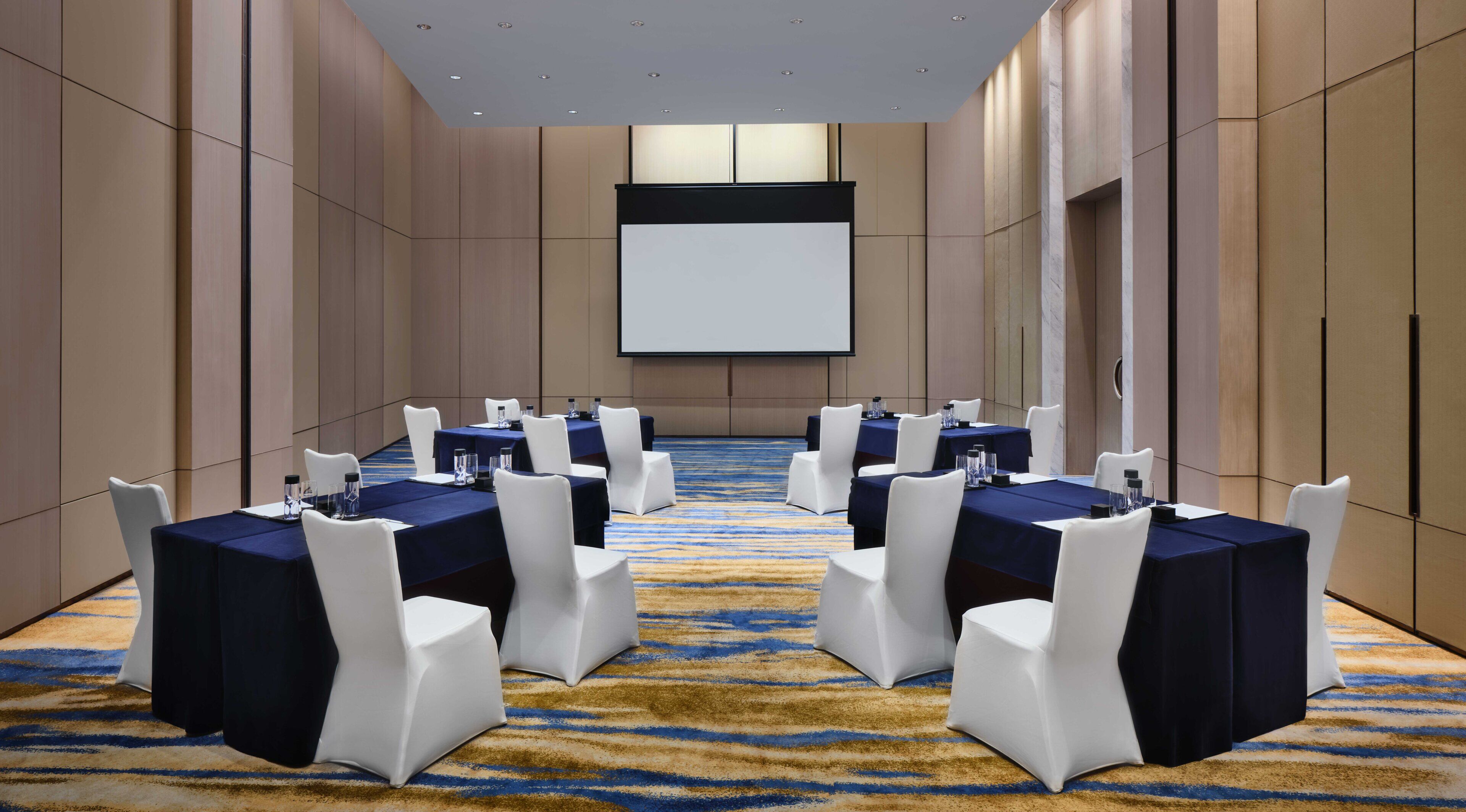 A conference room with a large screen, multiple tables, and chairs.