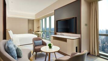 Une chambre d’hôtel avec un lit, deux fauteuils, une petite table, un téléviseur et une vue sur la ville.