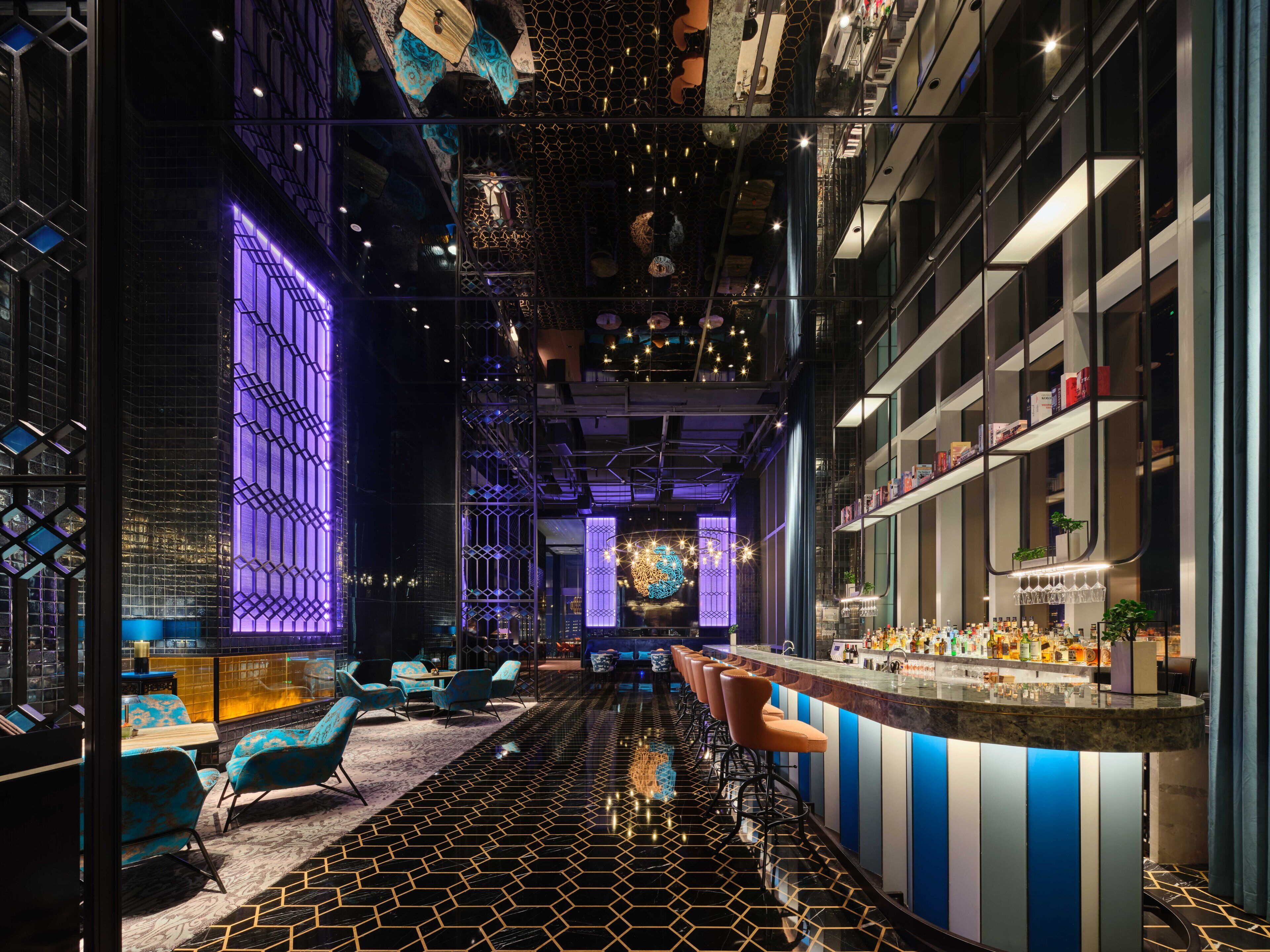 A modern bar area with a long counter, seating, and a decorative ceiling.