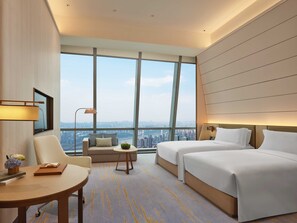 A modern hotel room with a large window offering a city view, a sofa, two beds, a small table, and a desk. - InterContinental Chongqing Raffles City by IHG (Chongqing)