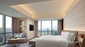 Habitación de hotel moderna con una cama grande, un sofá, una mesita y vistas a la ciudad.