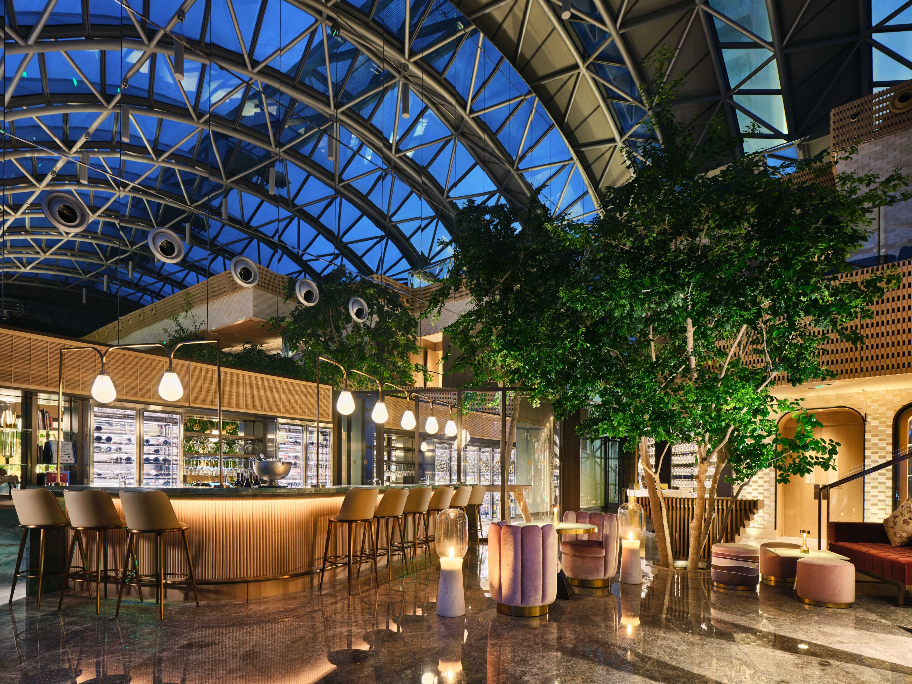 A modern interior with a bar area, seating, and a glass ceiling structure.