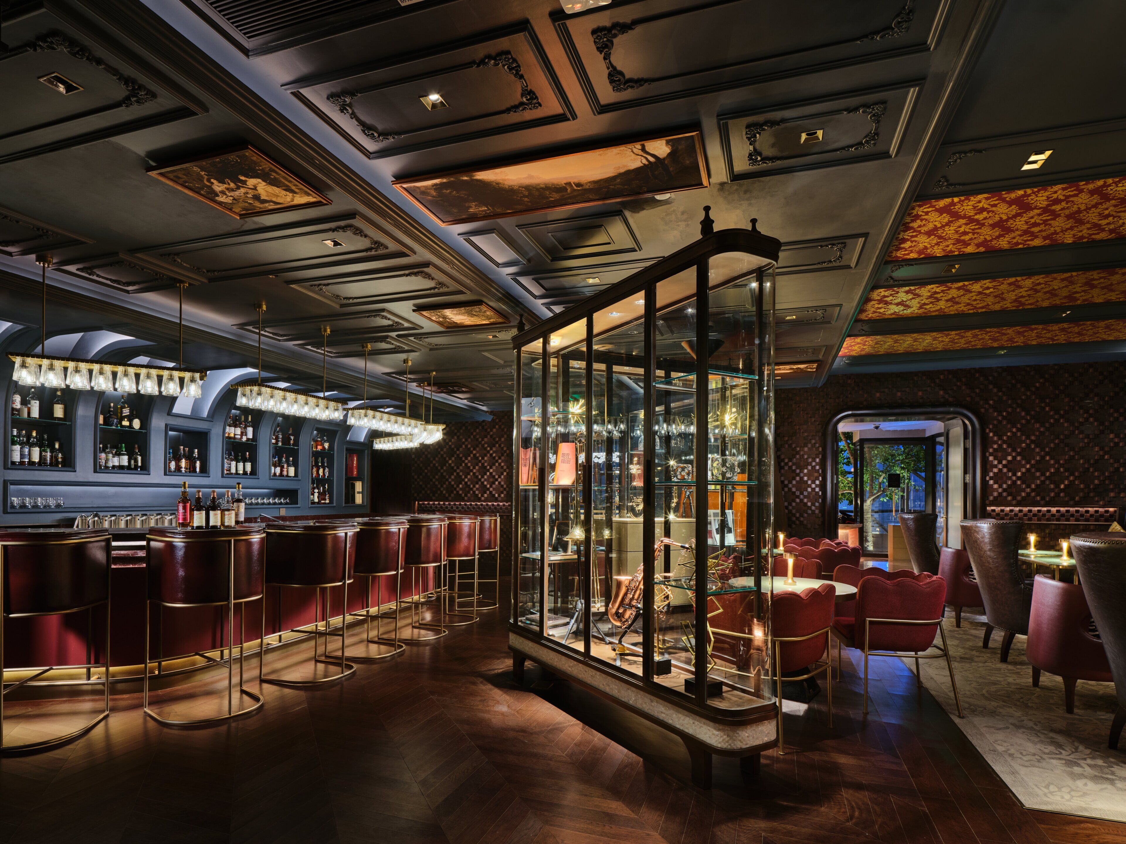 A bar area with a glass enclosure, red seating, and a patterned ceiling.