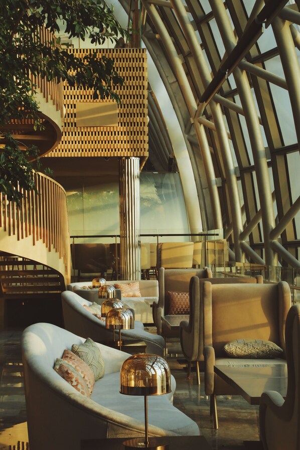 A modern interior with a curved ceiling, seating areas, and a staircase with a wooden railing. - InterContinental Chongqing Raffles City by IHG (Chongqing)