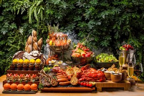 A table with various food items, including seafood, bread, and fruits, set against a backdrop of lush greenery. - InterContinental Chongqing Raffles City by IHG (Chongqing)