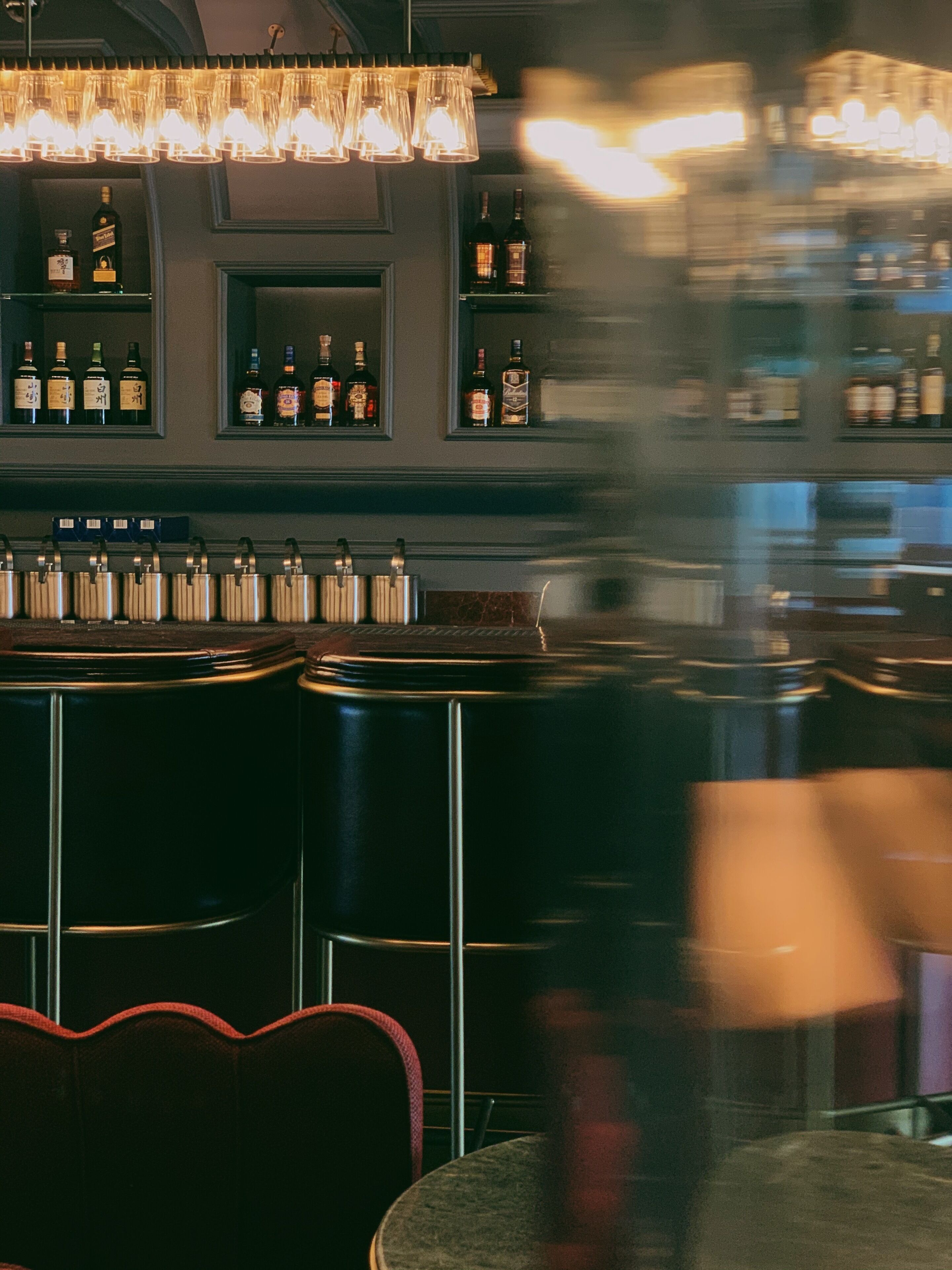 A bar area with shelves of bottles, a chandelier, and bar stools.