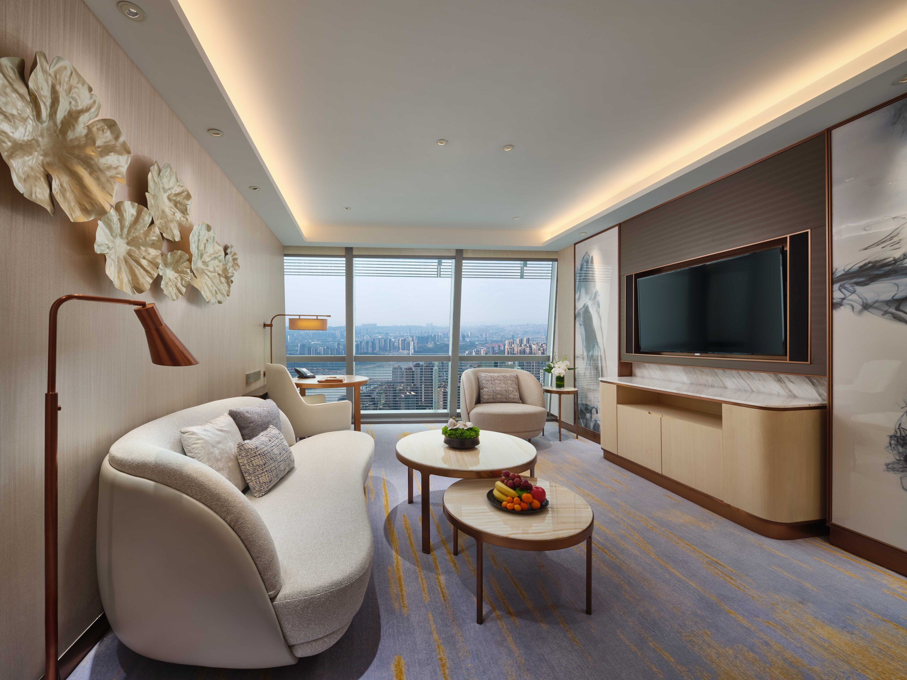 Una habitación de hotel moderna con sofá, mesa de centro y televisor. La habitación tiene un ventanal con vistas a la ciudad.