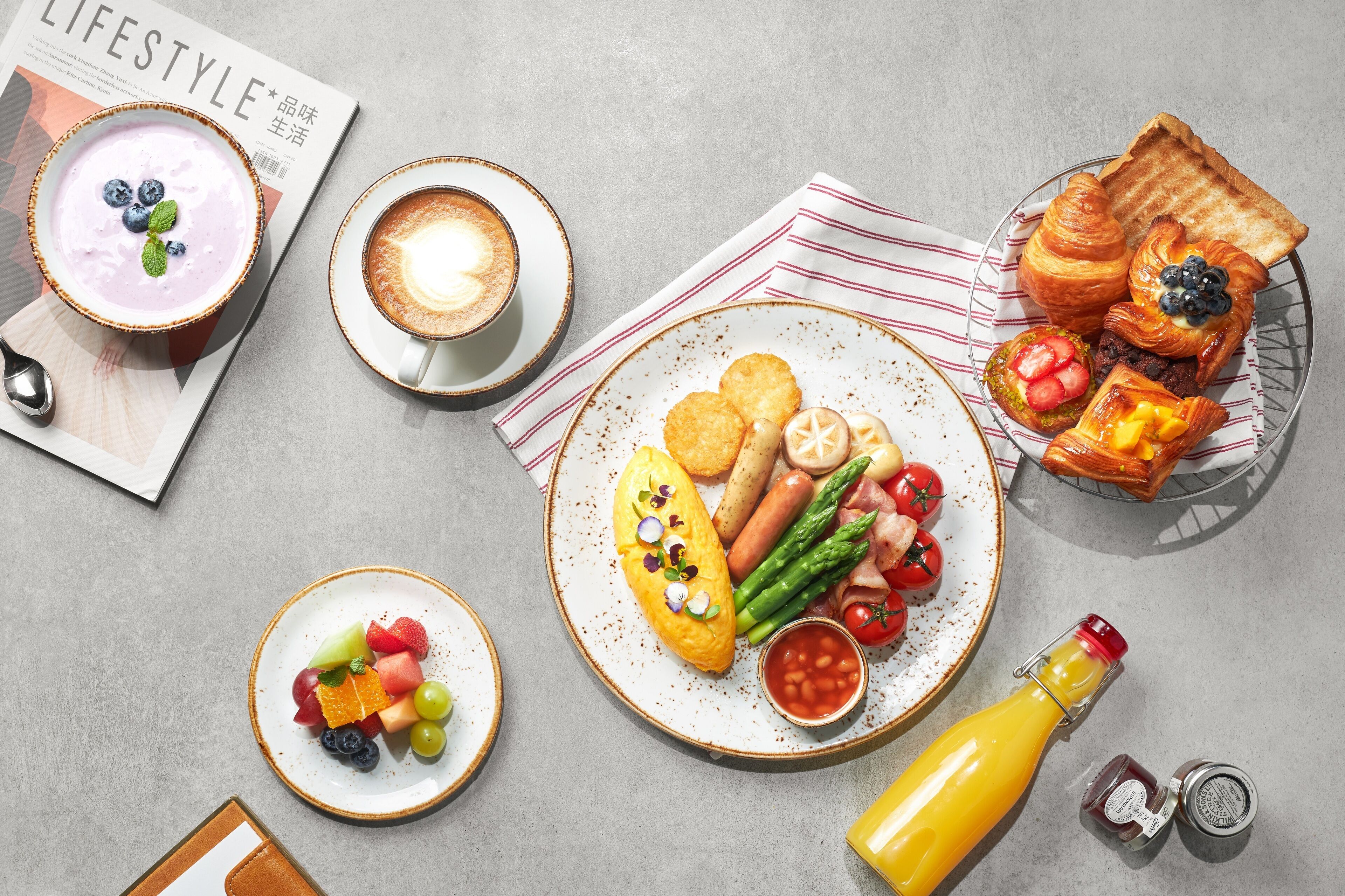 Uma mesa de café da manhã com diversos pratos, uma revista e uma garrafa de suco.