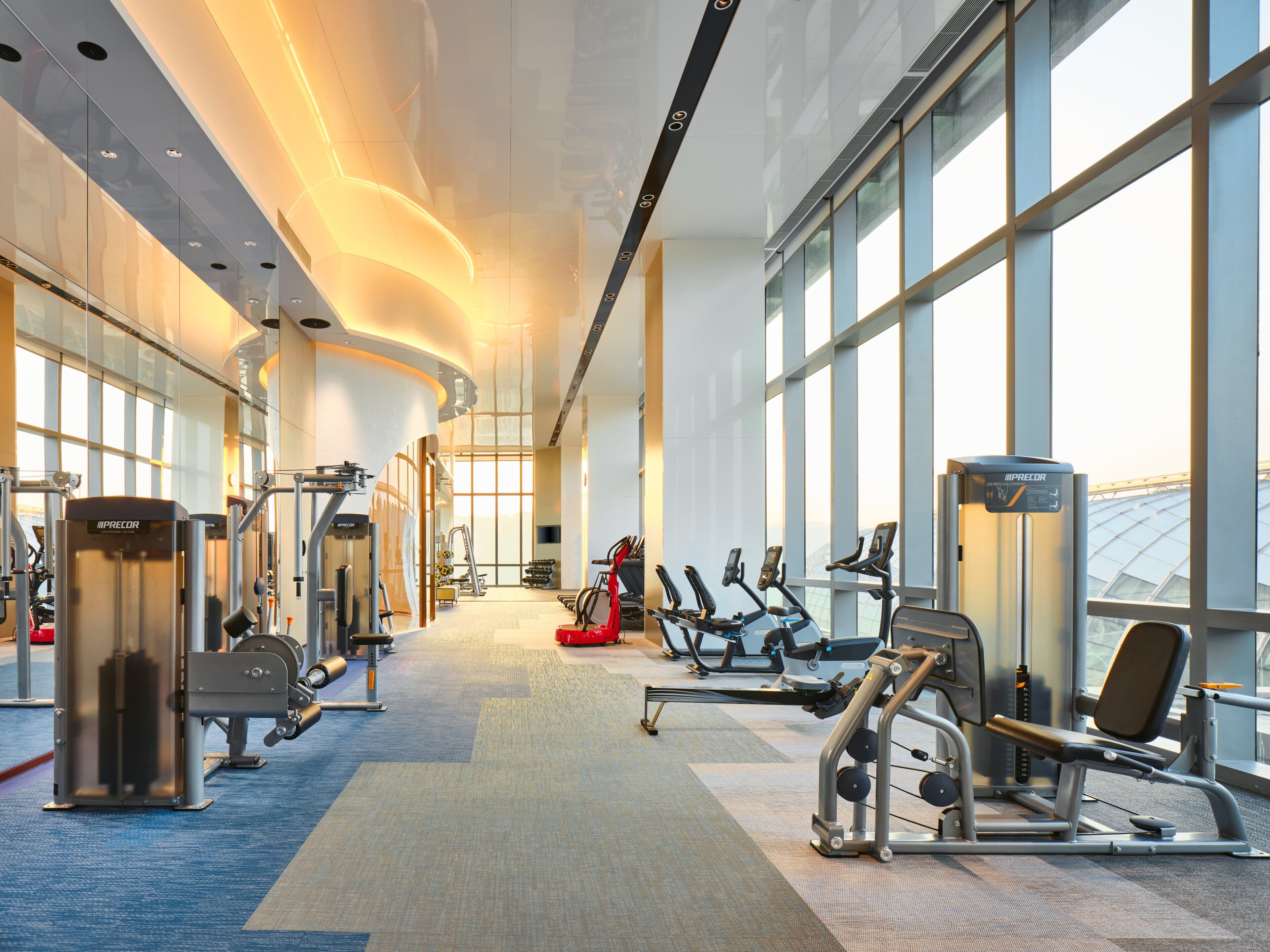 A modern gym with various exercise equipment, large windows, and a spacious layout.