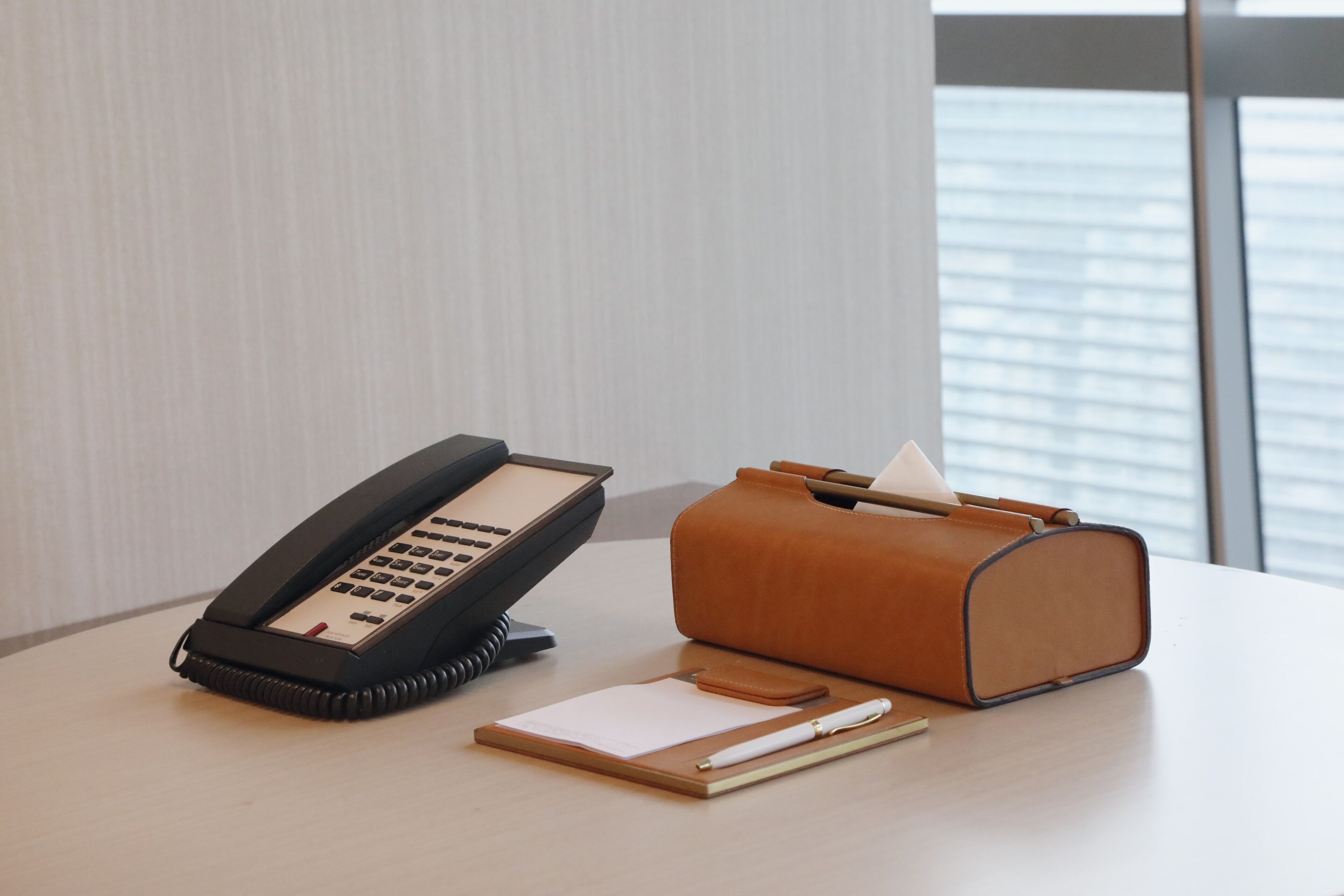 A desk with a telephone, a leather case, a notepad, and a pen.