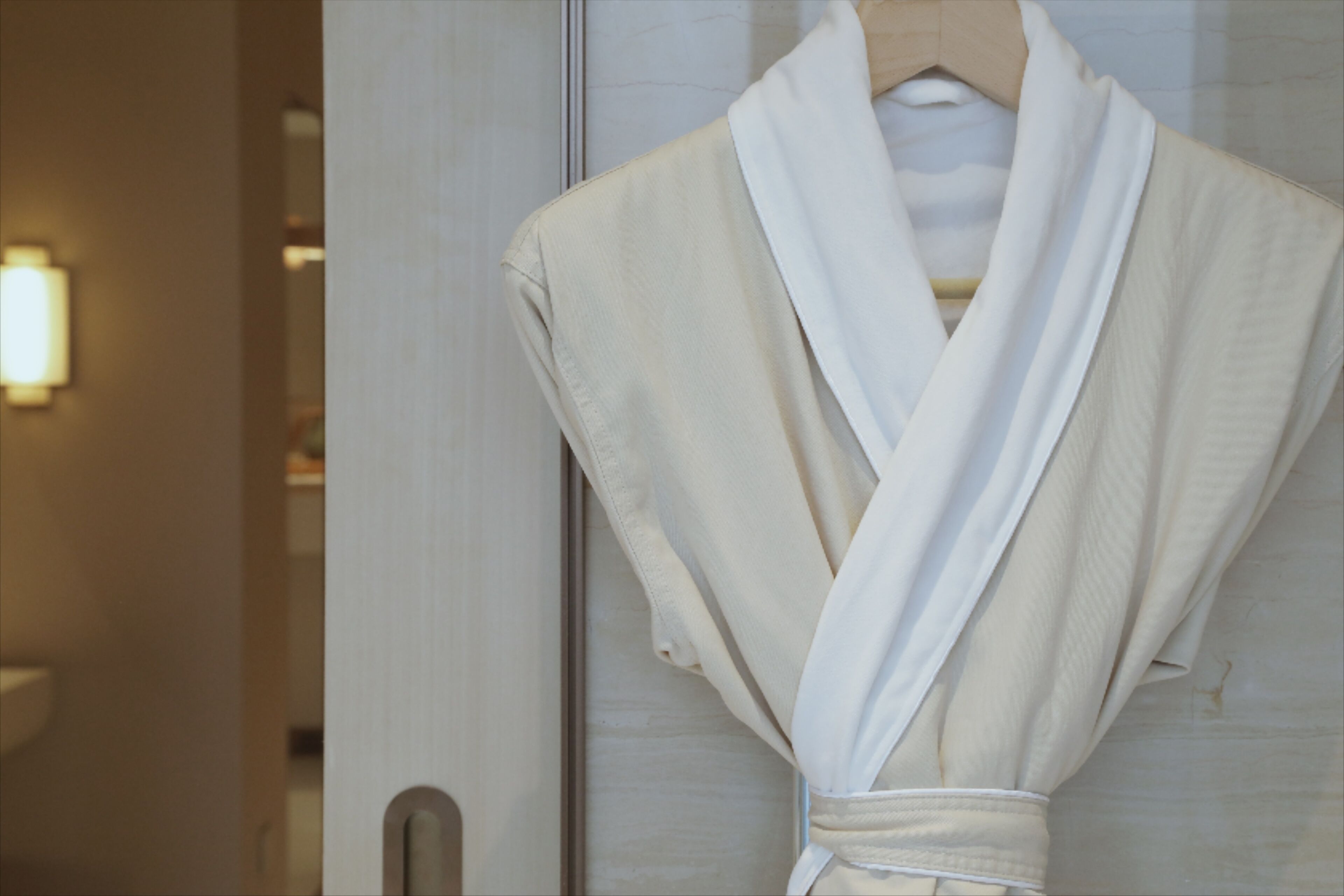 A white robe hanging on a wooden door in a hotel room.