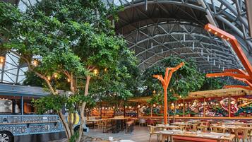 Un comedor interior con mesas, sillas y un árbol grande.