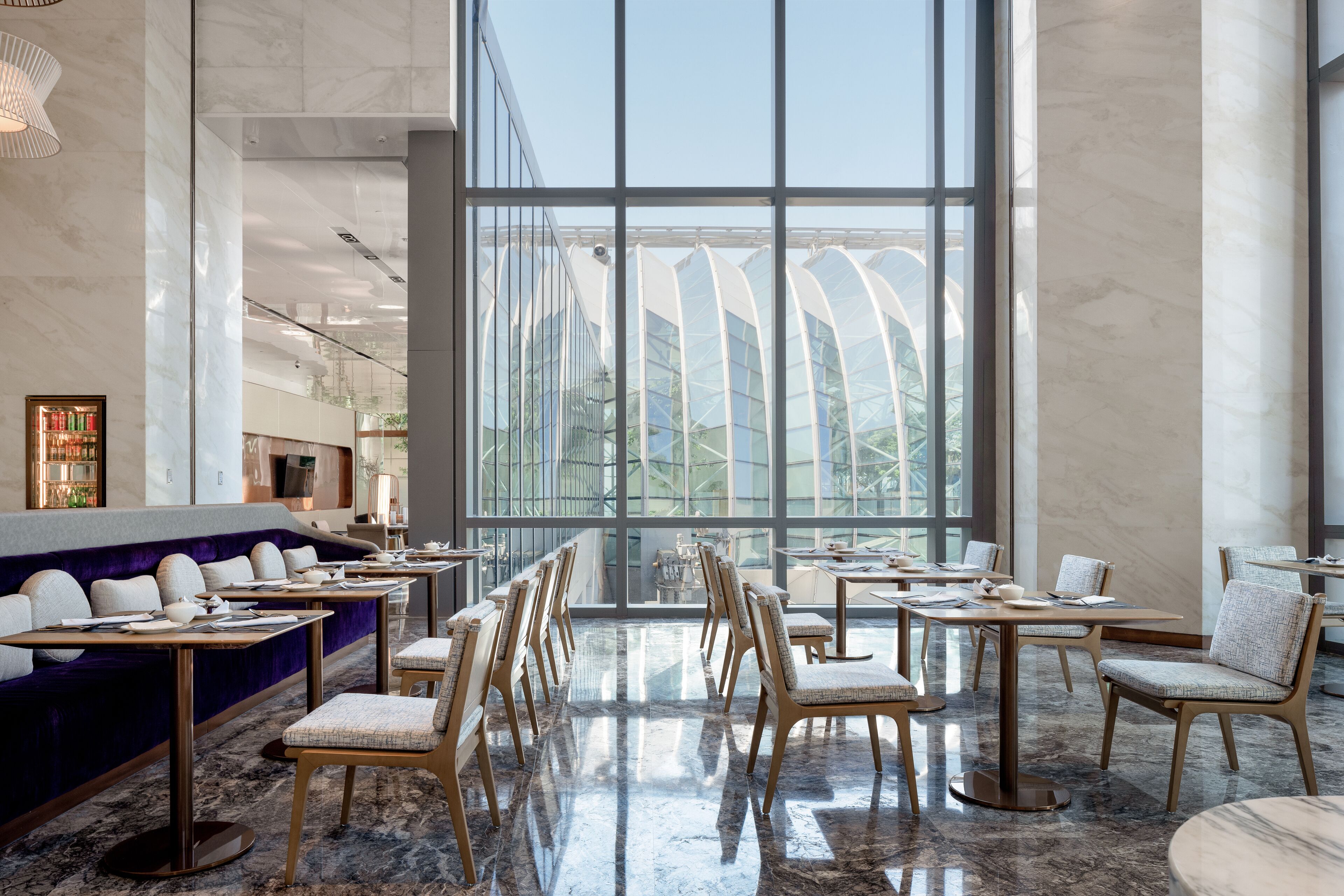 Een ruim restaurant met hoge plafonds, grote ramen en modern meubilair.