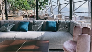 Un área de estar moderna con sofá y sillones, ventanas amplias y vistas al exterior.