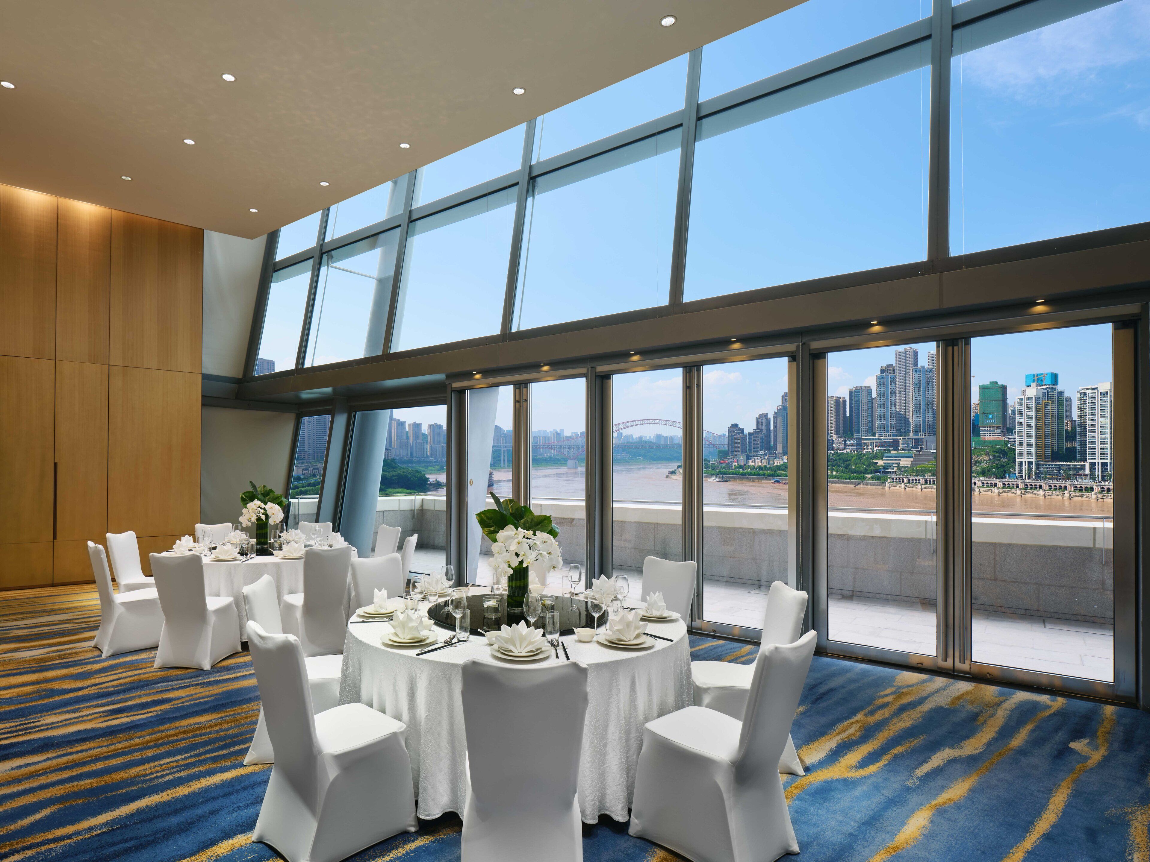 A conference room with round tables set for a meeting, large windows offering a city view, and a carpeted floor.
