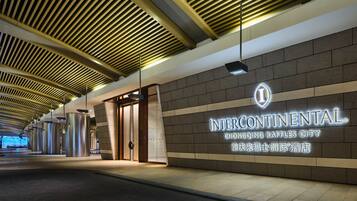 A corridor with a modern ceiling design, a wall with illuminated signage for Intercontinental Chongqing Raffles City, and a door leading to a room.
