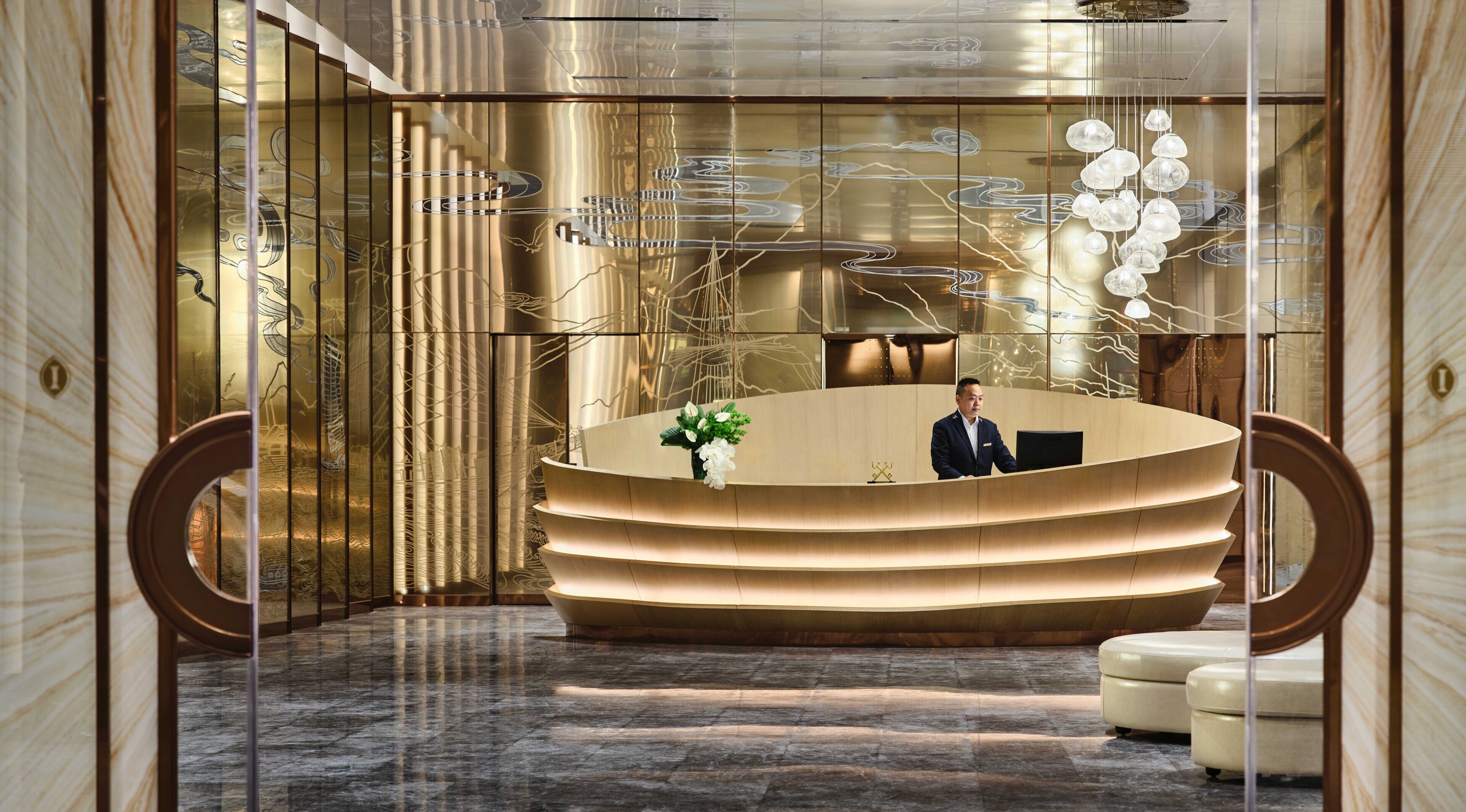 A reception area with a modern design, featuring a curved reception desk, a receptionist, and a decorative light fixture.