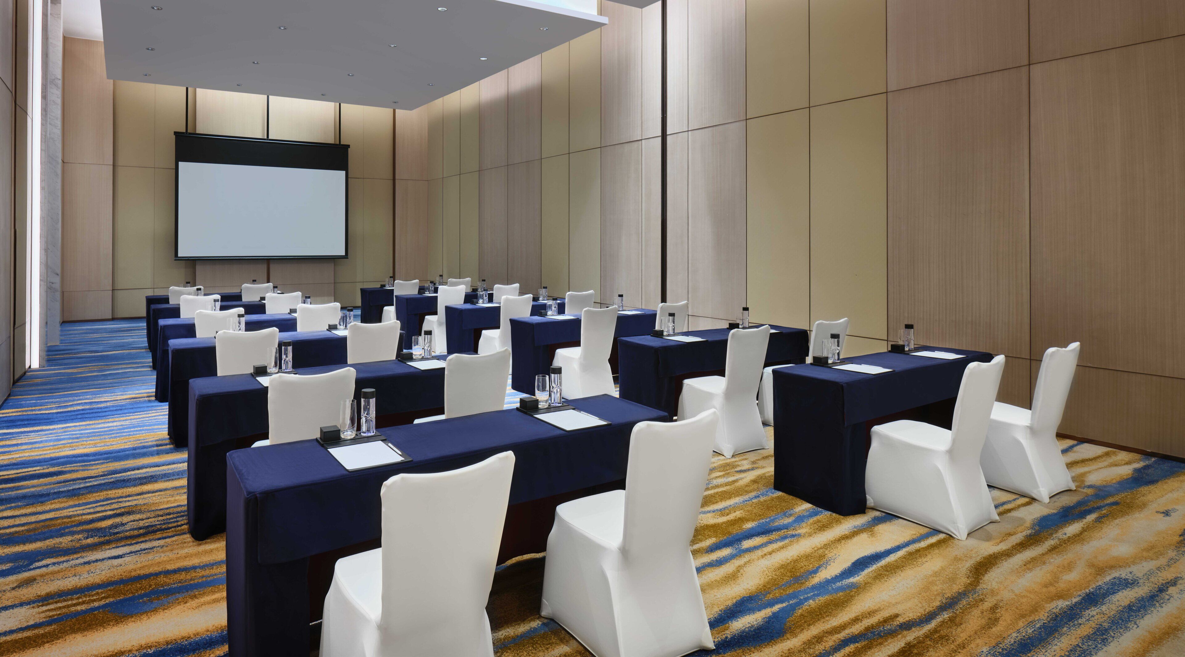 A conference room with multiple tables, white chairs, and a projector screen.