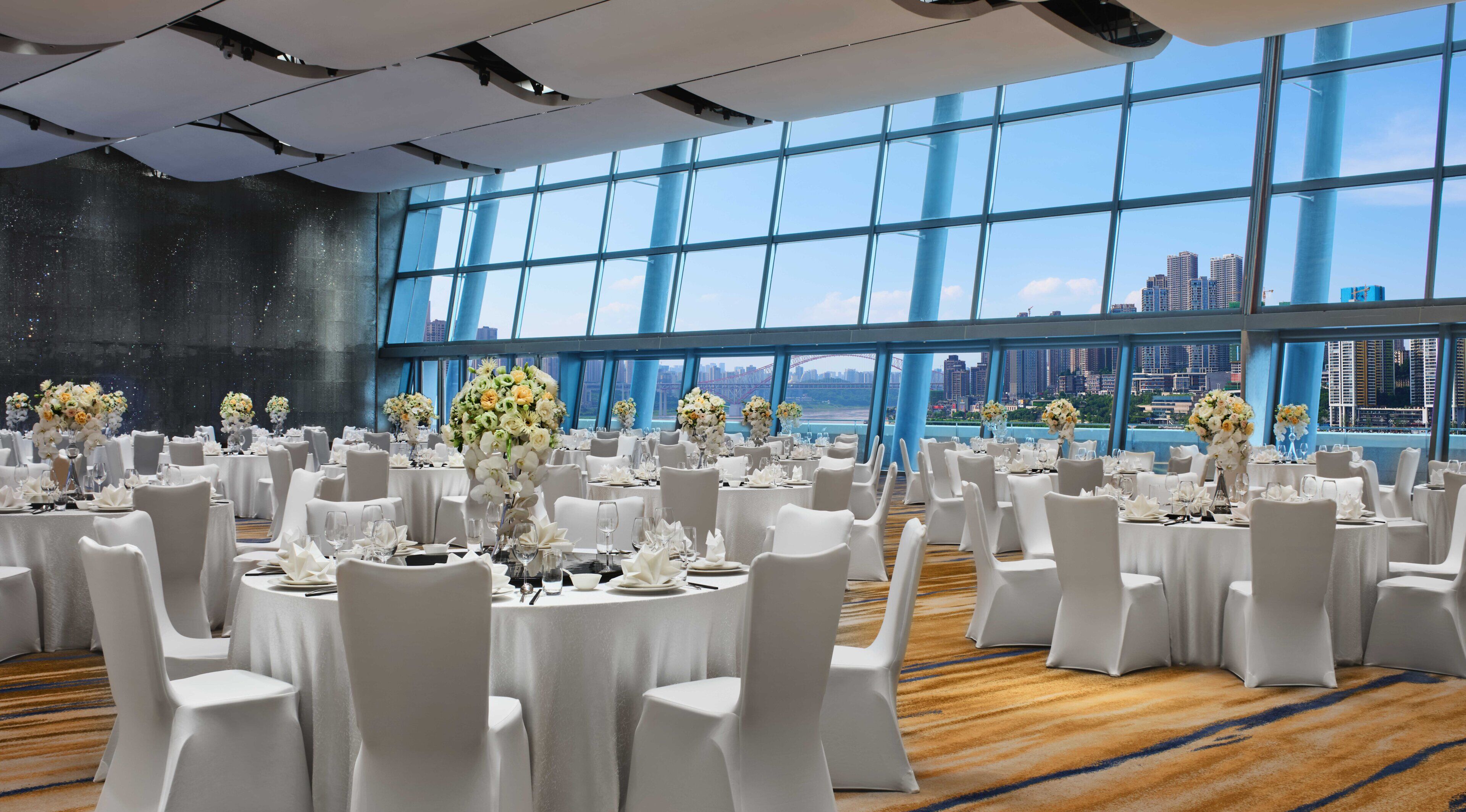 A banquet hall with round tables set for dining, white chairs, and floral centerpieces.