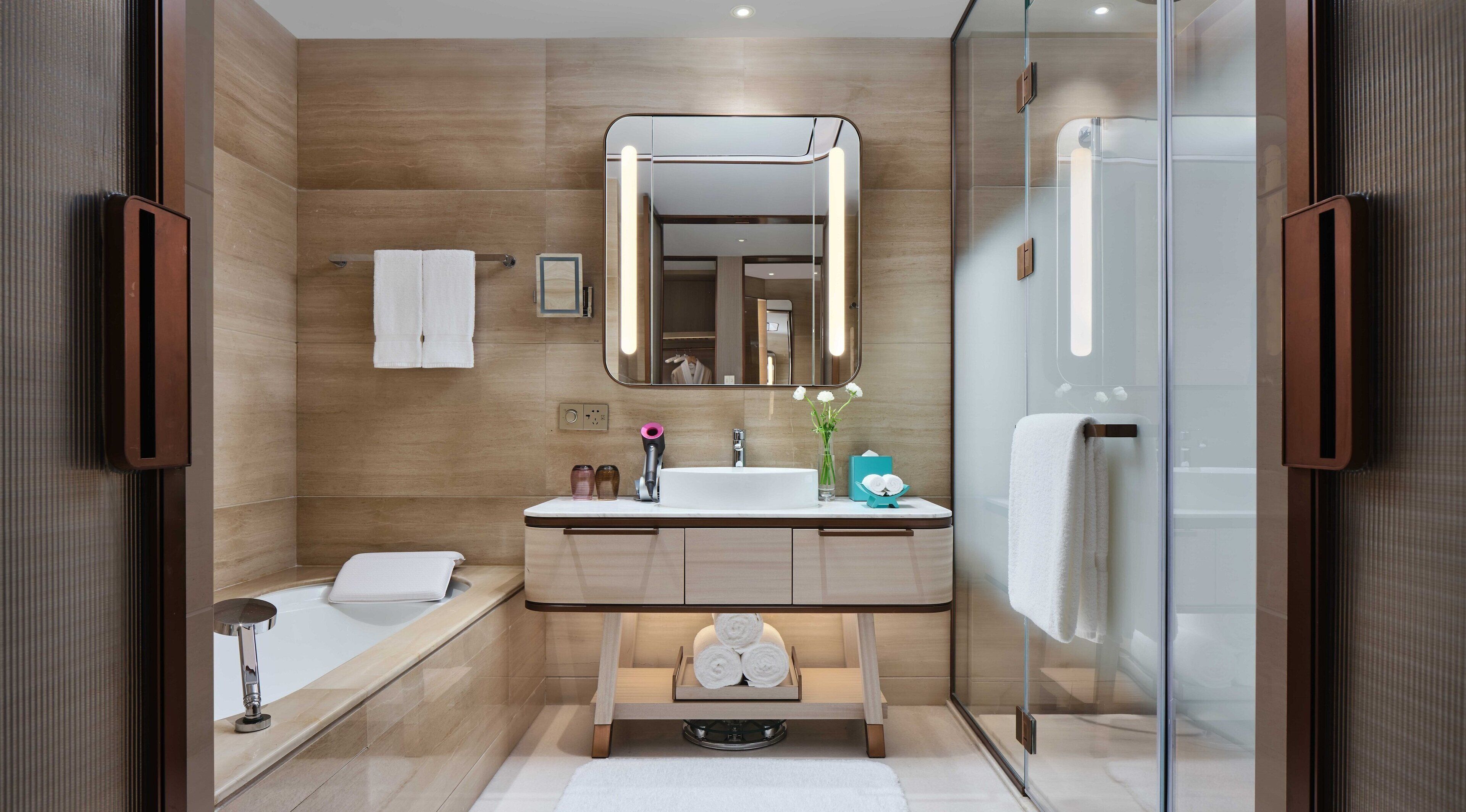 A modern bathroom with a large mirror, a bathtub, and a glass shower enclosure.