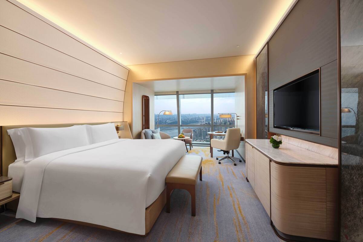 A modern hotel room with a large bed, a desk, a TV, and a city view.