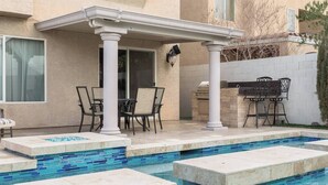 A pool with blue mosaic tiles, a covered patio area with chairs and a table, and a barbecue grill. - CASA MIA - Las Vegas traditional Luxury (Las Vegas)