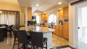 A spacious kitchen with granite countertops, wooden cabinets, and a central island with bar stools. - CASA MIA - Las Vegas traditional Luxury (Las Vegas)