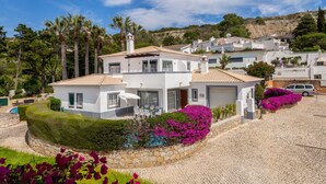 A white villa with a tiled roof, a stone wall, and a cobblestone driveway.